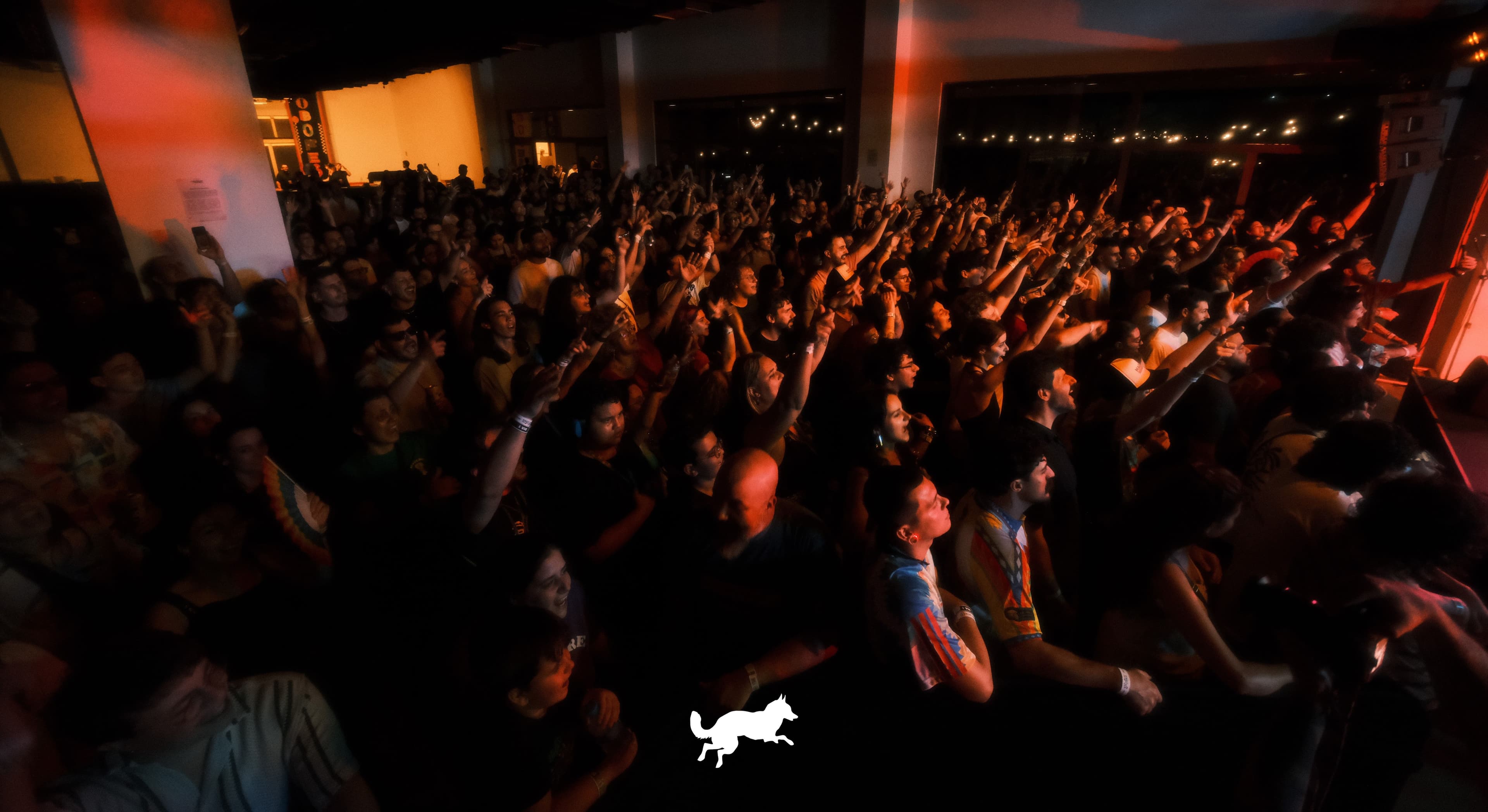 Público reunido durante apresentação musical, com braços levantados e iluminação avermelhada, em registro do Lobofest na Cidade 2026.